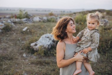 Bir anne, huzurlu bir günbatımında genç kızını manzaralı bir ortamın arka planına sevinçle sarılır..