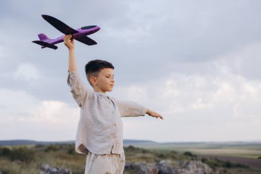 Uçsuz bucaksız bir arazide oyuncak bir uçakla oynayan genç bir çocuk, bulutlu bir gökyüzünün altında çocukluk merakı ve hayal gücünün bir örneğiydi..