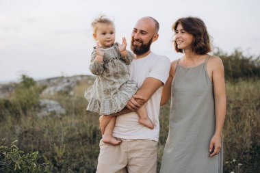 Neşeli bir aile dışarıda kaliteli zaman geçiriyor. Bir baba, genç kızını kucağında tutarken anne de yanında durur. Doğada bir anlık mutluluğu paylaşır..