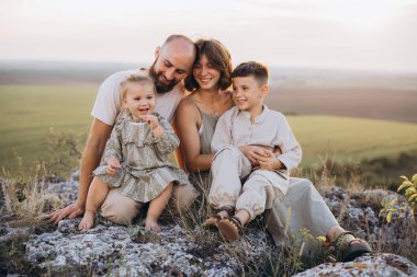 Neşeli bir aile, dışarıda güzel doğal bir manzarayla çevrili, gülümseyen çocuklar ve birbirini seven ebeveynlerle vakit geçiriyor..