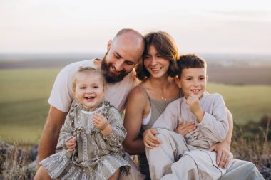 Dört kişilik neşeli bir aile, güzel bir manzarada mutlu bir anı paylaşıyor. Gülümseyen ebeveynler ve çocuklar birlikte kaliteli zaman geçiriyorlar..