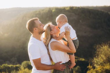 Mutlu aile birlikte dışarıda vakit geçiriyor. Güneşli bir günde anne babalar bebeklerine sarılıp gülümsüyor..