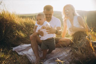 Neşeli bir aile güneşli bir günün tadını çıkarıyor, ebeveynler bebekleriyle oynuyor. Doğadaki mutluluk ve birliktelik anları yakalıyor..