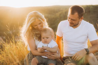 Üç kişilik neşeli bir aile güneşli bir arazide birlikte vakit geçiriyorlar. Ebeveynler ve çocuklar altın saat boyunca doğanın sıcaklığının ve güzelliğinin tadını çıkarıyorlar..