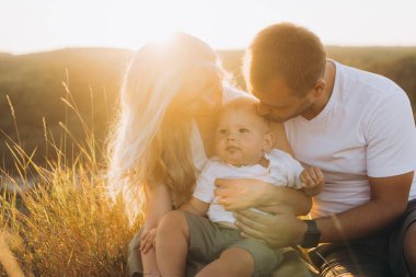 Sevgi dolu bir aile, doğada sıcaklığı, birlikteliği ve mutluluğu kucaklayan güneşli bir çayırda bebeğiyle mutlu bir anı paylaşır..