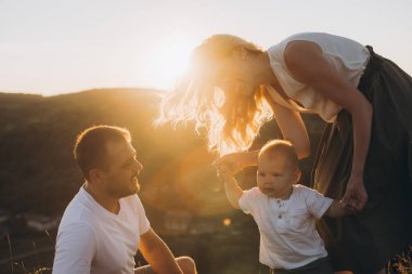 Neşeli aile anı gün batımında çekildi, gülümseyen ebeveynler ve yeni yürümeye başlayan çocuklar. Sıcak güneş ışığı dışarıda sakin bir atmosfer yaratır. Aile sevgisi ve birliktelik teması için mükemmel..