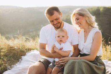 Neşeli bir aile anı, gülümseyen ebeveynler ve bebekleriyle piknik battaniyesinde güneşli bir günün tadını çıkarırken çekildi..