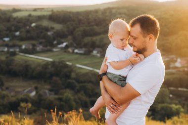 Bir baba gün batımında güzel bir kırsal alanda durup aile bağlarını ve doğanın huzurunu ön plana çıkarırken oğlunu sevgiyle kucağına alır..