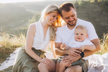 Neşeli bir aile, güzel bir açık havada birlikte vakit geçiriyor. Ebeveynler ve çocuklar piknik battaniyesinde oturup güneşin ve doğanın tadını çıkarıyorlar..