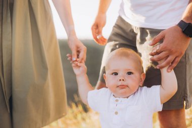 Parkta güneşli bir günde anne babasıyla el ele tutuşan sevimli bir bebek aile bağlarını ve geçimini simgeliyor..
