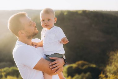 Bir baba gün batımında bebeğini sevgi dolu bir şekilde açık havada tutar. Sıcaklık ve bağlılık örneği olur. Aileyi ve doğayı yakalamak için mükemmel bir zaman..