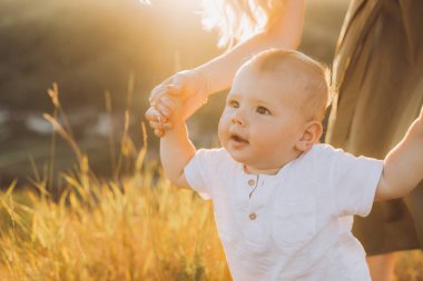 Gün batımında altın bir tarlada anne-baba tarafından desteklenen beyaz tişörtlü sevimli bir bebek sıcaklığı ve aile bağlarını yakalıyor..