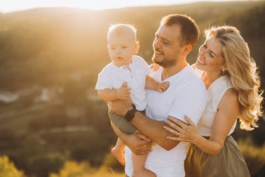 Ebeveynleri ve bebeğiyle mutlu bir aile, sıcak günbatımının tadını çıkarıyor, neşeli duyguları yakalıyor ve kırsal alanda aşk yaşıyor..