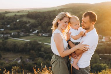 Üç kişilik neşeli bir aile sevgiyle kucaklaşırken gün batımında manzaranın tadını çıkarıyor. Doğanın huzurunu, birlikteliğini ve sevgiyi simgeliyor..
