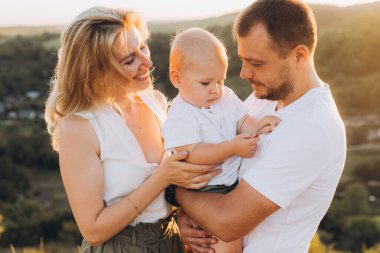 Mutlu bir aile anı. Anne babalar sıcak gün batımında sevgileriyle bebeğini kucaklar. Güzel bir doğal ortamda mutluluğu ve birlikteliği gösterir..