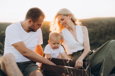 Neşeli bir aile, doğada güneşli bir günün tadını çıkaran bir baba, anne ve bebeğe ev sahipliği yaparak birlikte dışarıda kaliteli zaman geçiriyor..