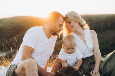 Gün batımında bebeğiyle huzurlu bir anın tadını çıkaran sevgi dolu bir aile. Ebeveynler çocuklarıyla bir bağ paylaşıyor, sıcak ve neşeli bir ortam yaratıyorlar..