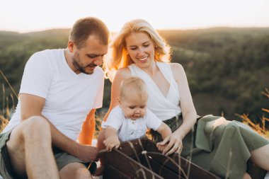 Neşeli bir aile bebekleriyle güneşli bir günün tadını çıkarıyor. Gün batımında doğal bir ortamda neşeli anlar yaratıyorlar..