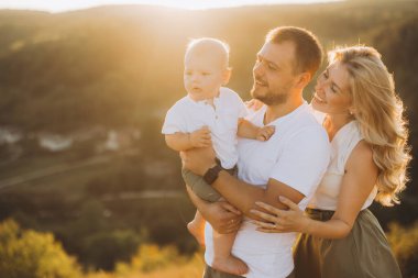 Üç kişilik neşeli bir aile, bir baba, anne ve bebek, güneşli bir günde açık havada eğleniyorlar, mutluluk ve beraberlik anları yakalıyorlar..