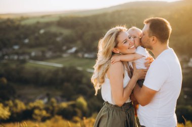 Neşeli bir aile, gün batımında manzaralı bir kırsal alanda kucaklaşarak dışarıda sevgi dolu bir anı paylaşır. Mutluluğun, sevginin ve aile bağlarının mükemmel bir temsili..