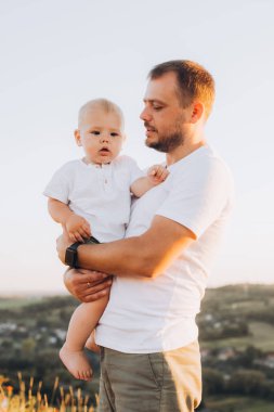 Bir baba gün batımında dışarıda dururken bebeğini sevgiyle kucağına alır. Doğadaki iç açıcı aile anını yakalar..