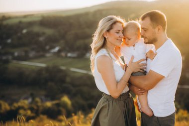 Üç kişilik mutlu bir aile, güzel bir altın saat gün batımında, sıcaklığı ve birlikteliği yakalayan kırsalda sevgiyle kucaklaşır..