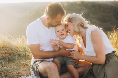 Neşeli bir aile güneşli bir çayırda hassas bir anı paylaşır. Aileler gülümseyen oğullarını kucaklarlar. Doğaları gereği güzel ve keyifli bir yaz gününde..     