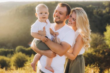 Üç kişilik neşeli bir aile açık havada güneşli bir günün tadını çıkarıyor, aşk, mutluluk ve aile bağlarını doğal bir ortamda yakalıyor..