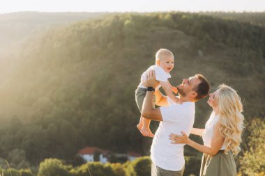 Neşeli bir aile, güneşli bir doğal ortamda bebeğiyle dışarıda oynuyor. Huzurlu bir ortamda sevgi ve mutluluğu yakalıyor..