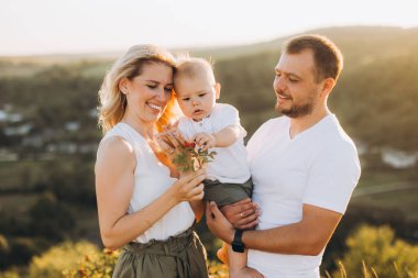 Mutlu aile doğada birlikte güzel zaman geçiriyor. Anne, baba ve erkek bebek güneşli bir günde güzel manzarayı keşfediyorlar. Huzurlu bir ortamda neşeli bir bağ ve aşk.