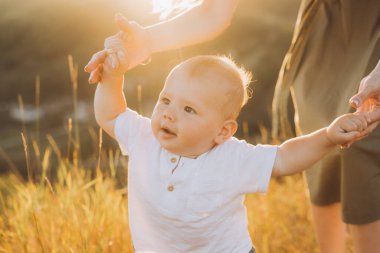 Neşeli bir bebek, güneşli bir tarlada bir yetişkinin elini tutarak altın saat boyunca neşeli bir anı yakalıyor. Sıcak ışık mutluluğu ve aile bağını vurgular..