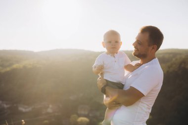 Bir baba çocuğunu sevgiyle kucağına alır ve huzurlu bir günbatımının tadını çıkarır. Doğal bir ortamda, aile sevgisinin ve bağının özünü yakalar..