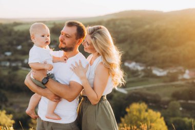 Gün batımında dışarıda mutlu aile bağları. Ebeveynler çocuklarını manzaralı bir kırsalda kucaklıyor. Huzurlu, doğal bir ortamda sevgi ve sıcaklık yayıyorlar..