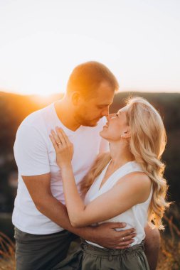 Bir çift gün batımında şefkat dolu bir kucaklaşmayı paylaşıyor, açık hava manzarasına karşı bir aşk ve samimiyet anı tasvir ediyorlar.