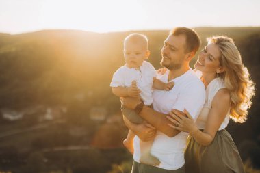 Neşeli bir aile bir tepenin üstünde duruyor, altın güneş ışığının tadını çıkarıyorlar. Ebeveynler ve çocuklar, açık havada geçirdikleri güzel bir anda paylaşılan sevgi ve sıcaklığı kucaklarlar..