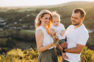 Doğada sevgi ve aile bağının özünü yakalayan mutlu ebeveynler ve küçük oğulları, güzel bir yamaçta gün batımında birlikte güzel vakit geçiriyorlar..