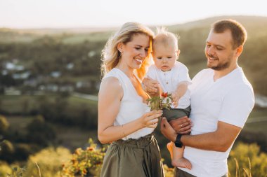 Neşeli bir aile birlikte güzel bir açık hava ortamında vakit geçiriyor. Ebeveynler ve bebekleri güneşin altında doğanın güzelliğinin tadını çıkarırlar..