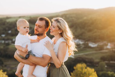 Üç kişilik neşeli bir aile gün batımında manzaralı bir ortamda kucaklaşıyor, kırsalda aşk ve beraberlik anları yakalıyor..