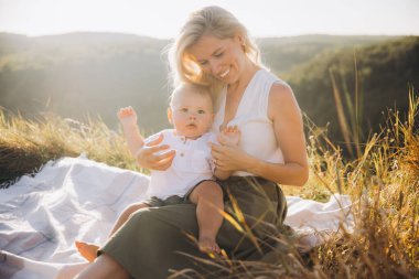 Mutlu bir anne ve bebeği piknik sırasında güneşli ve huzurlu bir günün tadını çıkarıyorlar. Sahne sıcaklığı ve aile bağını doğal bir ortamda yakalıyor..