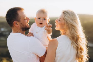 Neşeli bir aile, dışarıda güzel vakit geçiriyor. Gülümseyen bir bebek ve ebeveynleri var. Güneşli ve huzurlu bir ortamda aşkı, mutluluğu ve birlikteliği yakalamak..
