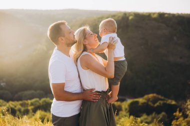 Neşeli bir aile açık havada güneşli bir günün tadını çıkarıyor. Ebeveynler gülümsüyor ve bebeklerini kucaklıyorlar, doğanın ve aile sevgisinin güzelliğini kucaklıyorlar..