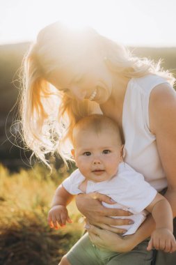 Işıl ışıl bir anne, güneşli bir günde bebeğini güneşin öptüğü bir tarlada tutarak sevgisini, sıcaklığını ve anneliğin özel bağını gösterir..