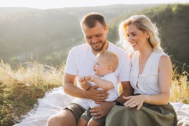 Neşeli bir aile dışarıda kaliteli zaman geçiriyor. Ebeveynler piknik battaniyesine oturup güneşin altında güneşleniyorlar..