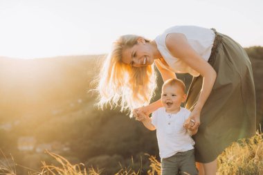 Neşeli bir anne ve küçük çocuğu güzel bir doğal ortamda güneşli bir anı paylaşıyor, mutluluğu ve aile bağlarını yansıtıyor..
