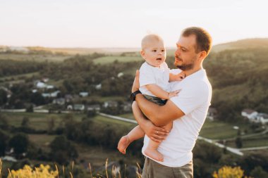 Bir baba bebeğini kucağında taşrada güzel bir günbatımının tadını çıkarıyor. Dışarıda sıcaklığı, sevgiyi ve aile bağlarını aktarıyor..