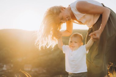 Neşeli bir anne doğada güneşli bir yürüyüş sırasında bebeğiyle vakit geçirir, gün batımında mutluluğun ve bağlantının özünü yakalar..