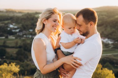 Mutlu bir aile, doğada sıcak bir günbatımının tadını çıkarıyor, küçük çocuklarını kucaklıyor. Açık havada güzel bir aşk ve birliktelik anı....