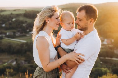 Sevgi dolu bir aile yaz günbatımında birlikte vakit geçirir. Ebeveynler, doğal güzelliklerle çevrili bir ortamda bebekleriyle sıcak bir kucaklaşmayı paylaşıyorlar..