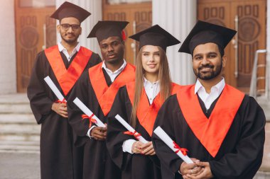 Bir grup gülümseyen mezun kep ve cübbe giyerek diplomalarını gururla taşıyorlar. Açık havada yakalanarak akademik başarılarını ve parlak geleceklerini kutluyorlar..