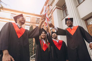 Neşe dolu mezunlar, prestijli bir üniversite binasının önünde diplomalarını yükselterek başarıyı ve yeni başlangıçları simgeliyorlar..